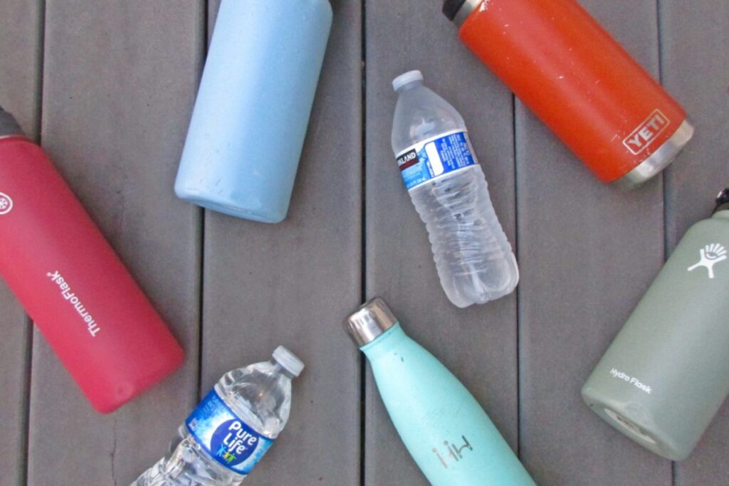 Reusable water bottles and disposable plastic bottles arranged on a wooden surface to compare sustainable and single-use drink containers.
